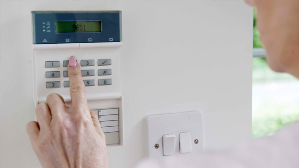 Woman Setting Control Panel On Home Alarm System